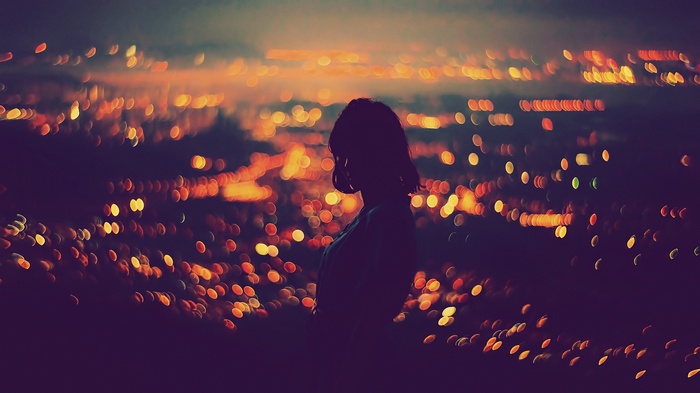 Silhouette of a woman against bokeh city lights at night
