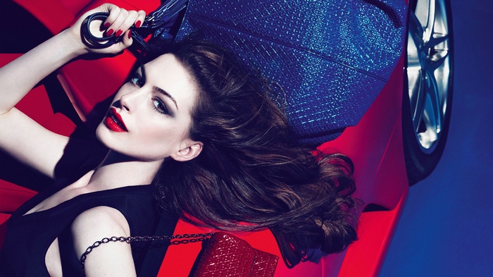 Anne Hathaway lying on a red car with a blue bag