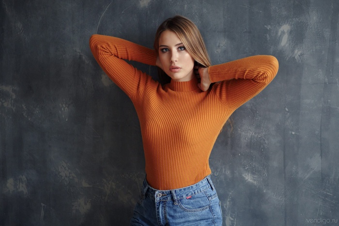 Woman with hands in hair wearing orange sweater and jeans