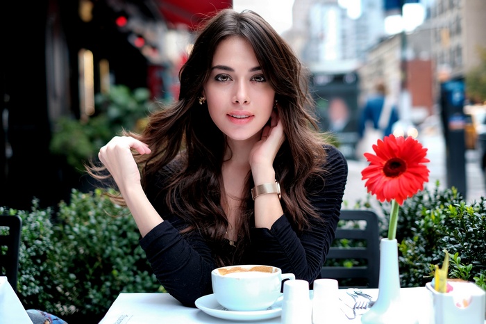 Woman with long brown hair at an outdoor cafe with coffee and a red flower