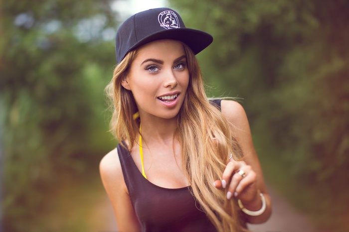 Woman with blonde hair wearing a black snapback and tank top