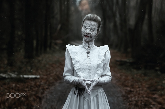 Woman in white dress with lace mask in forest