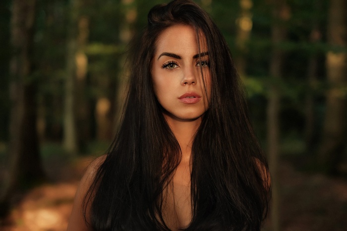 Woman with long dark hair and green eyes in a forest