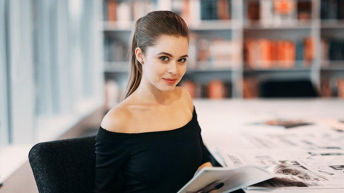Woman with ponytail in black top reading in library