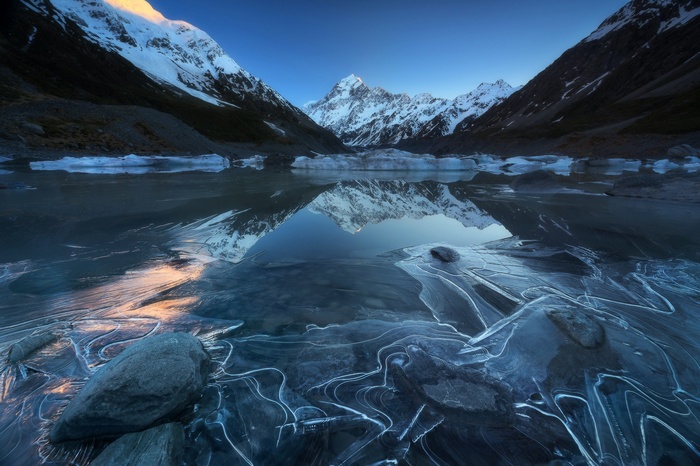 Frozen lake reflecting snow-capped mountains at sunrise