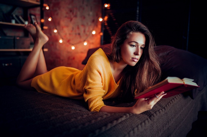 Woman in yellow sweater reading a book on a bed