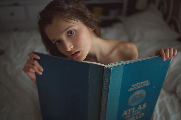 Girl reading National Geographic Atlas of the World in bed