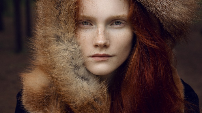 Close-up portrait of a redhead woman with blue eyes and freckles wearing fur