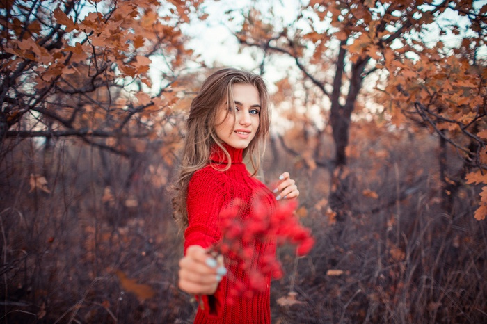 Woman in red sweater holding rowan berries in fall forest
