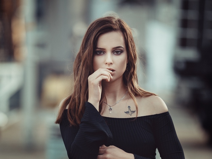 Woman with tattoo and necklace, finger on lips