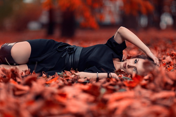Woman in black dress lying on autumn leaves