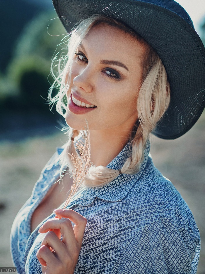 Woman in hat smiling, holding a wheat stalk