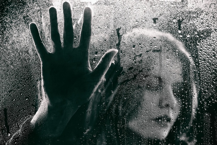 Woman's hand and face behind a wet window