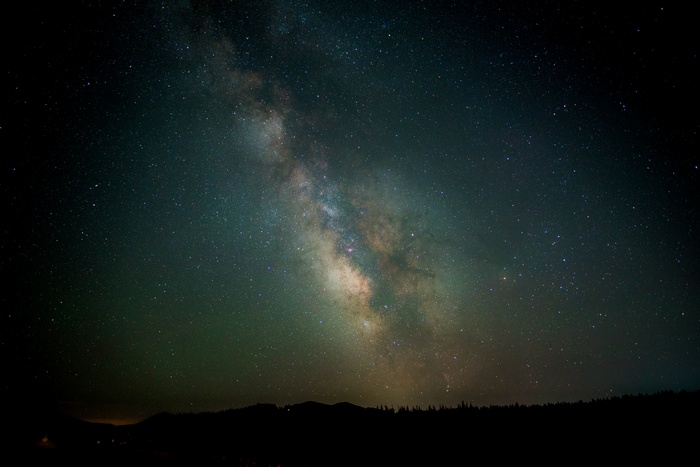 Milky Way galaxy over silhouetted trees and mountains