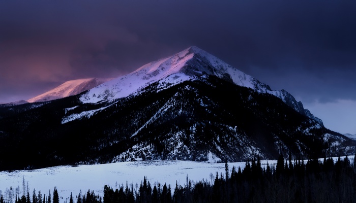Snow-covered mountain peak at dusk with dark clouds
