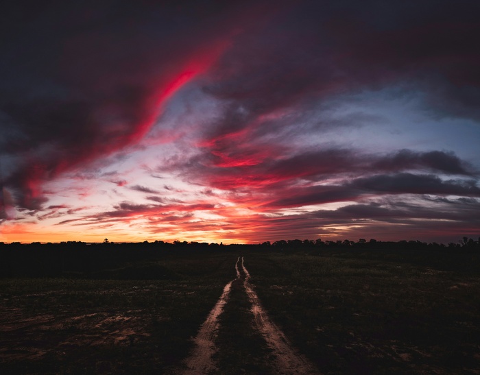 Dirt road through a field at sunset with dramatic clouds
