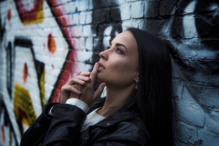 Woman with finger on lips in front of graffiti wall