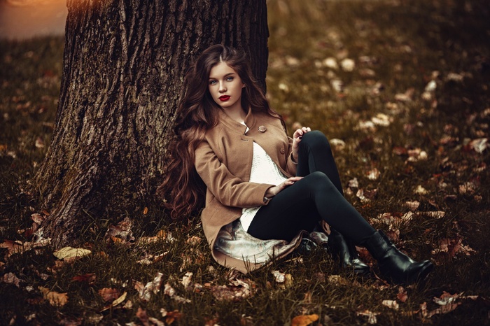 Woman with long brown hair sitting by a tree in fall