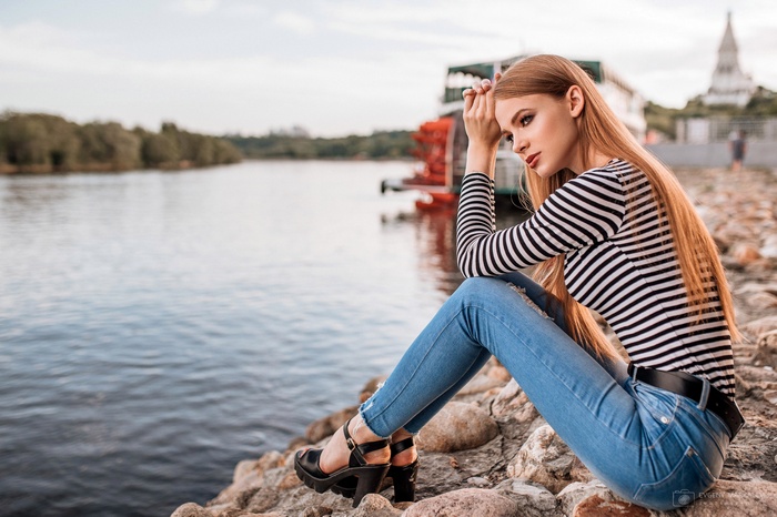 Woman in jeans and striped shirt sitting by the river