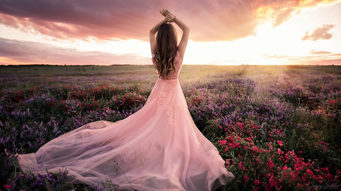 Woman in pink dress in a field at sunset