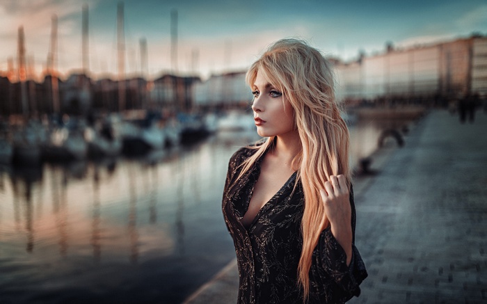 Woman with blonde hair in a black dress on a dock at sunset