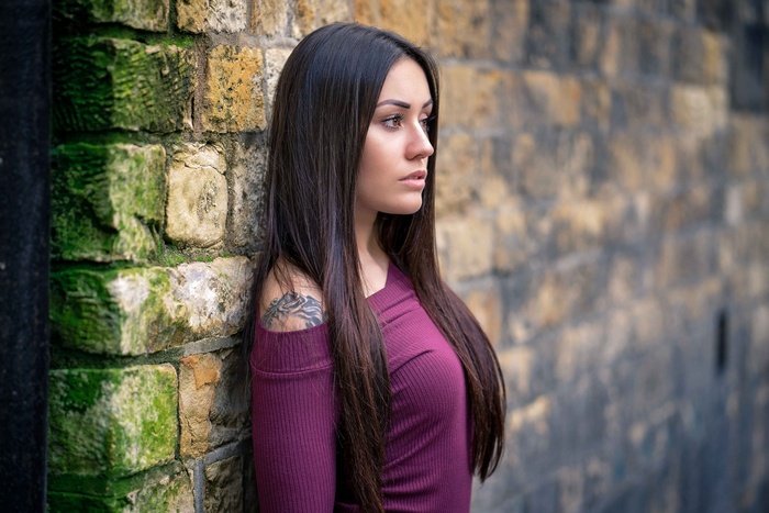 Woman with tattoo leaning against a brick wall
