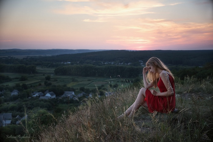 Woman in red dress sitting on grassy hill at sunset