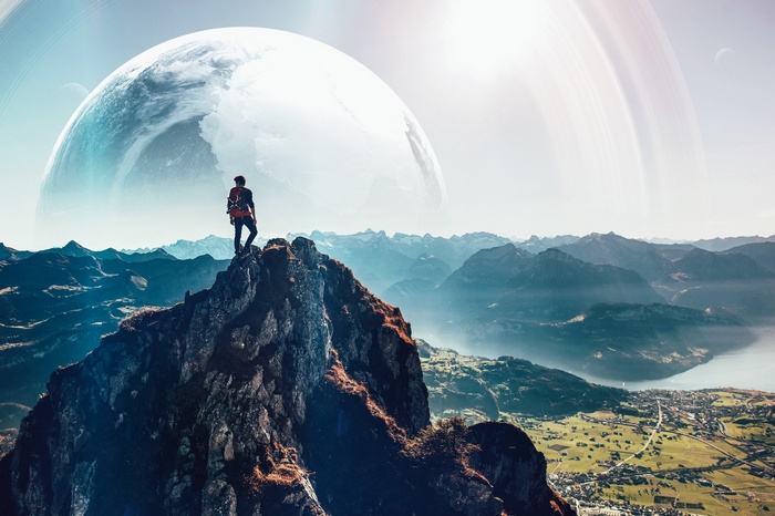 Man on mountain peak with planet and rings in sky