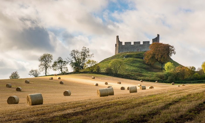 Castle ruins on a hill above a field of hay bales in Scotland