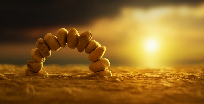 Stacked stones forming an arch on a sandy beach at sunset