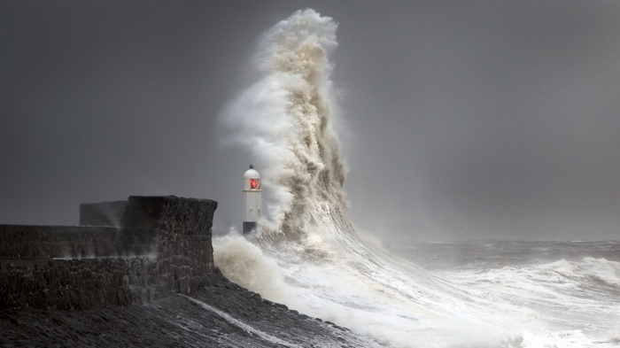 Massive wave crashing near lighthouse on stone wall in Wales