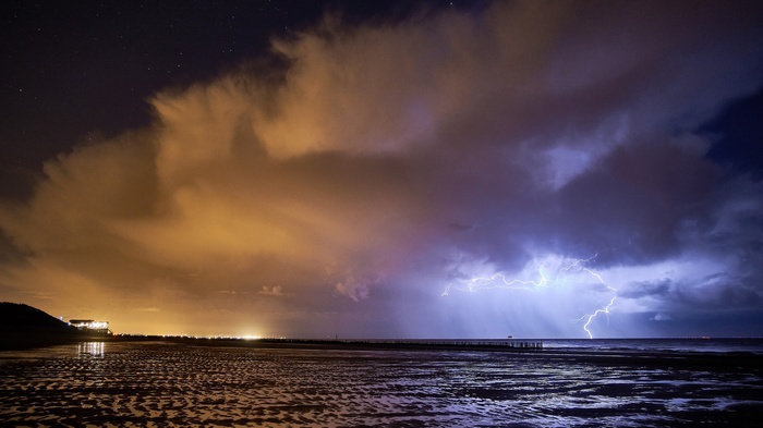 Lightning strikes over the sea at night with clouds and stars