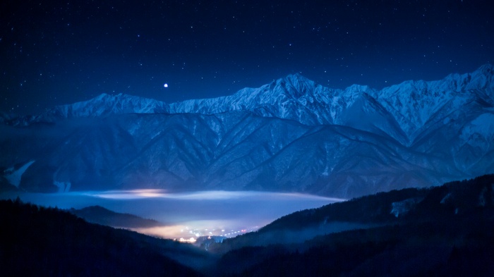 Starry night over misty mountains and valley lights
