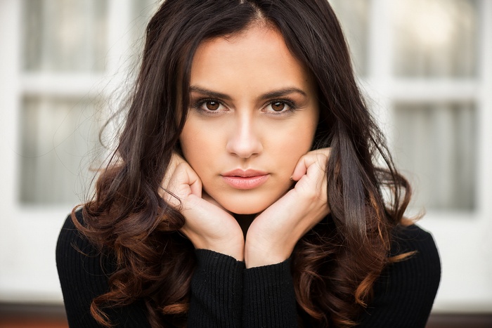 Woman with dark wavy hair and hands on chin