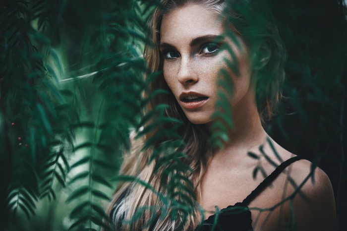 Woman with freckles behind green leaves