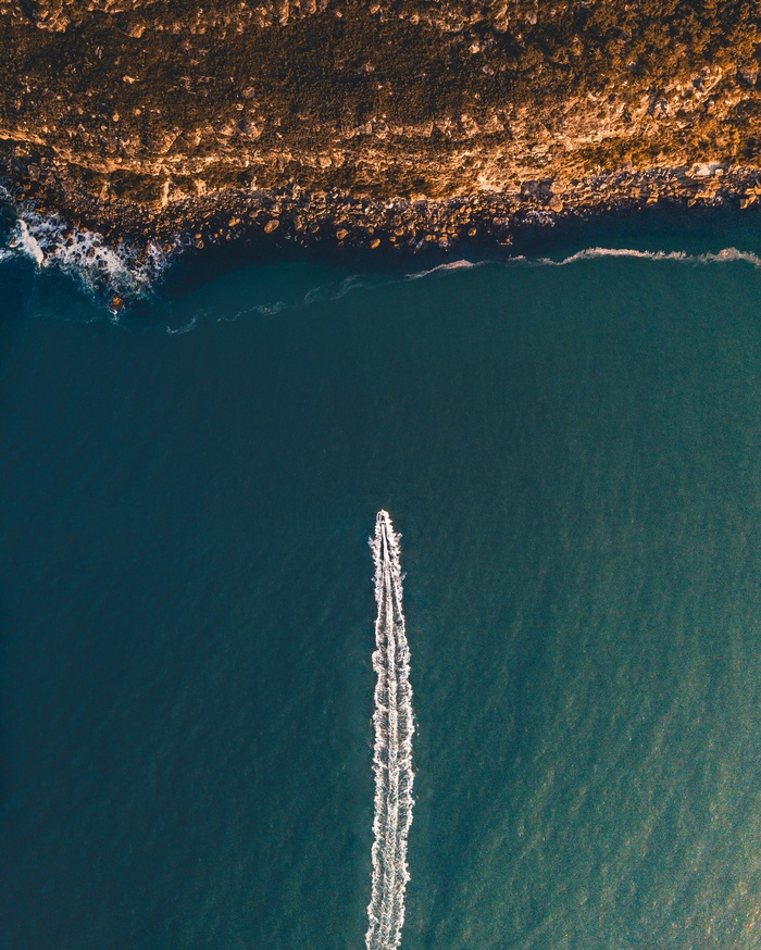 Boat leaving a wake near a rocky coastline