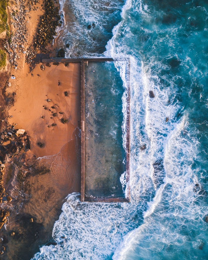 Aerial view of ocean waves crashing into a rock pool