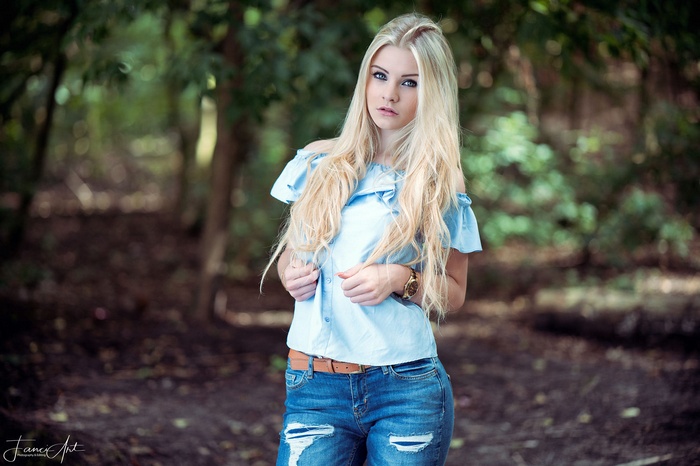 Blonde woman with blue eyes in torn jeans in forest