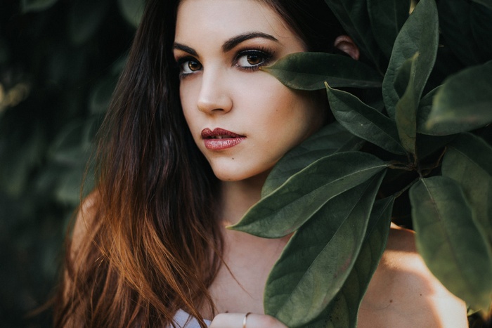 Woman with dark hair and makeup behind green leaves