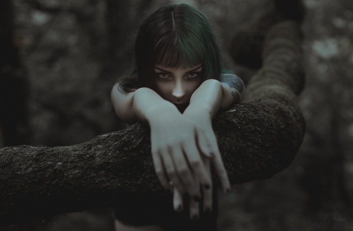 Woman with green hair leaning on a tree branch