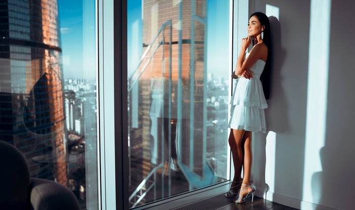 Woman in white dress by window with cityscape view