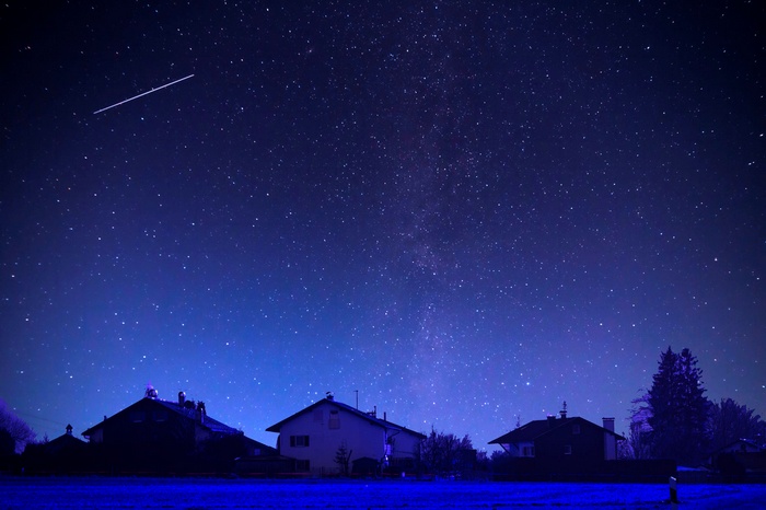 Starry night sky over houses with a meteor shower