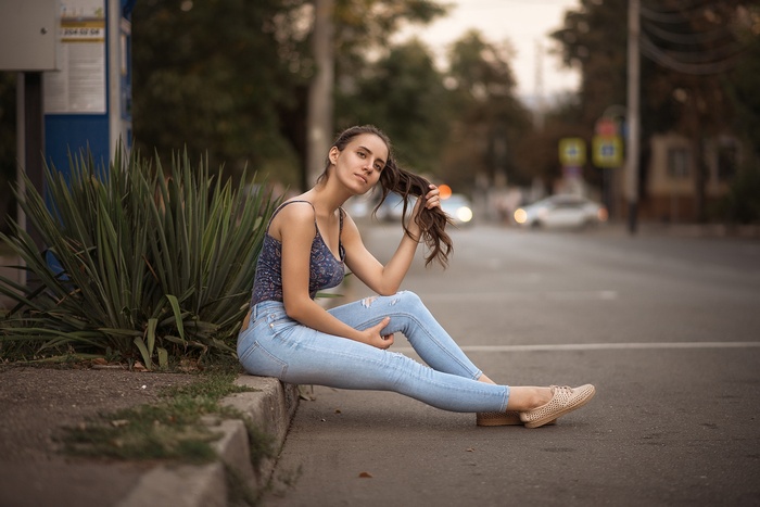 Woman sitting on curb with jeans and tank top