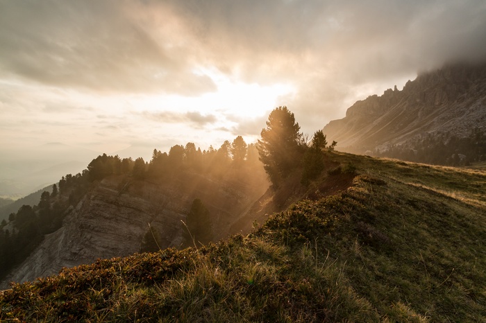 Sunlight beams through clouds over a mountain ridge with trees