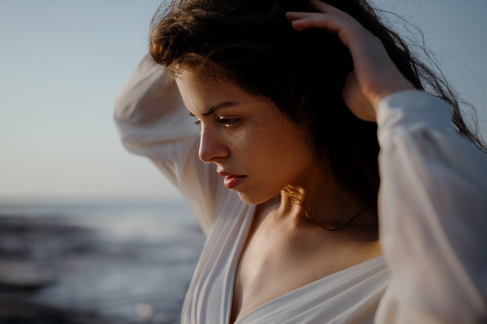 Woman with freckles and hands in hair outdoors