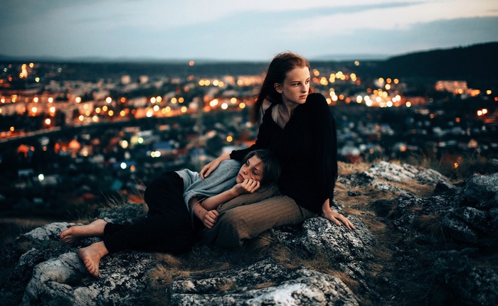 Two young women on a hill overlooking a city at night