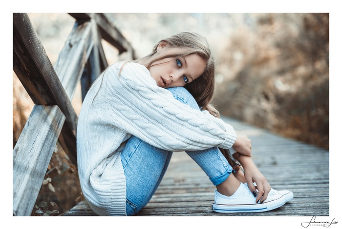 Young woman with blonde hair and blue eyes sitting on a wooden boardwalk