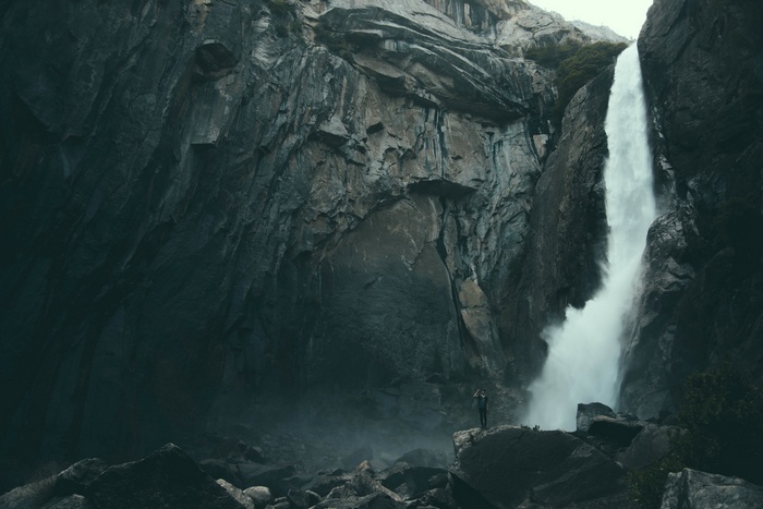 Man photographing a tall waterfall in a rocky canyon