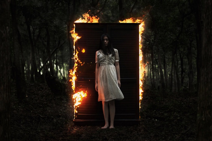 Woman in white dress standing in front of burning wardrobe in forest