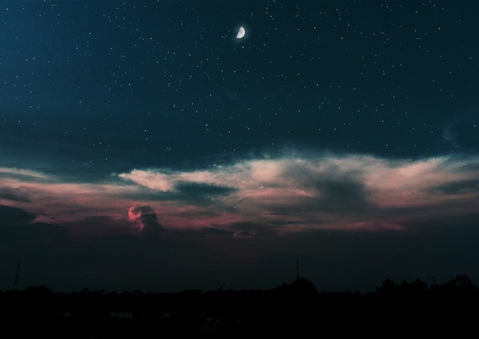 Starry night sky with moon and clouds over silhouette